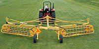 A yellow farm tractor with a hay rake on a green field.