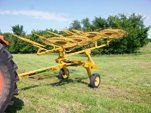 Yellow hay rake attached to a tractor in a grassy field on a sunny day.