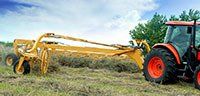 Orange tractor pulling a yellow hay rake across a grassy field under a blue sky.