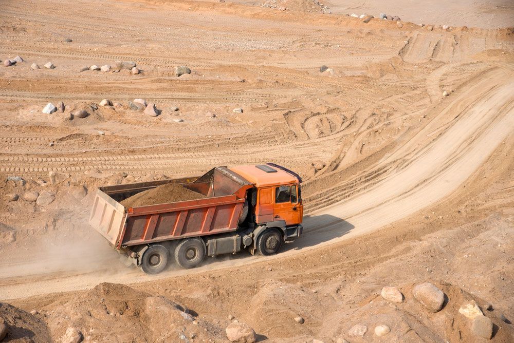 A Dump Truck Driving on a Sandy Road Carrying Dirt — Koumala Quarry In Koumala, QLD