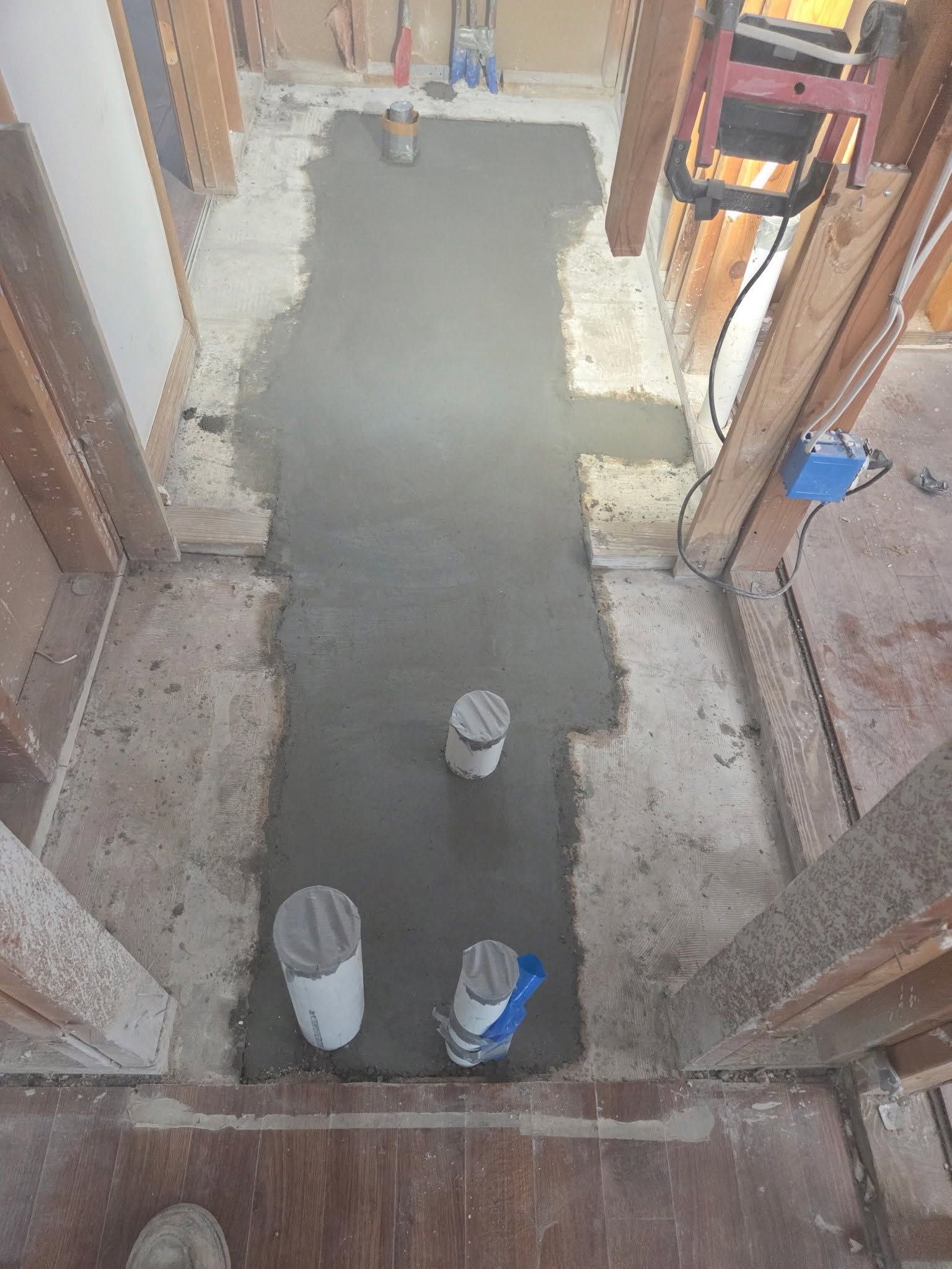 Partially poured concrete floor in a narrow hallway with exposed walls and pipes