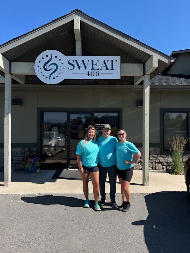 Three people stand in front of Sweat 406 gym entrance, wearing matching teal t-shirts and black shorts.