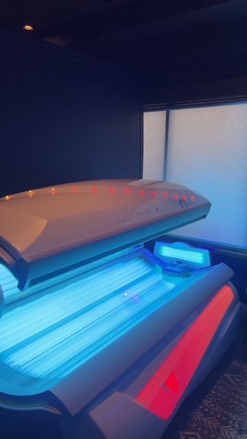 An open, indoor tanning bed with glowing blue UV lights inside a darkened room.