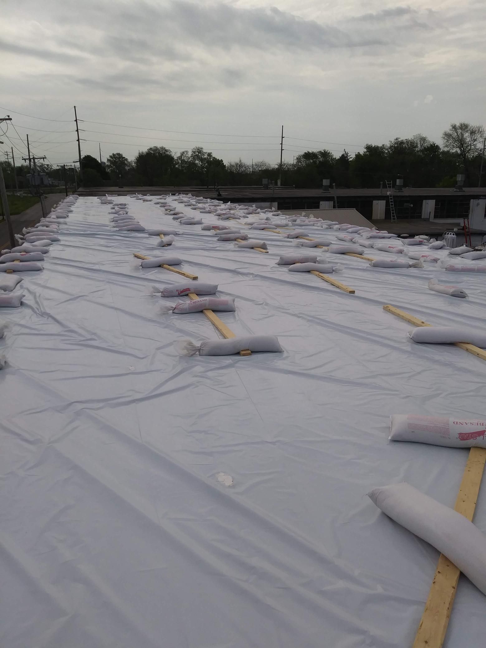 A large white tarp is being rolled up on a roof.