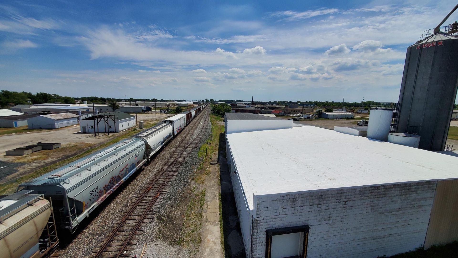 A train is going down the tracks next to a building with a white roof.
