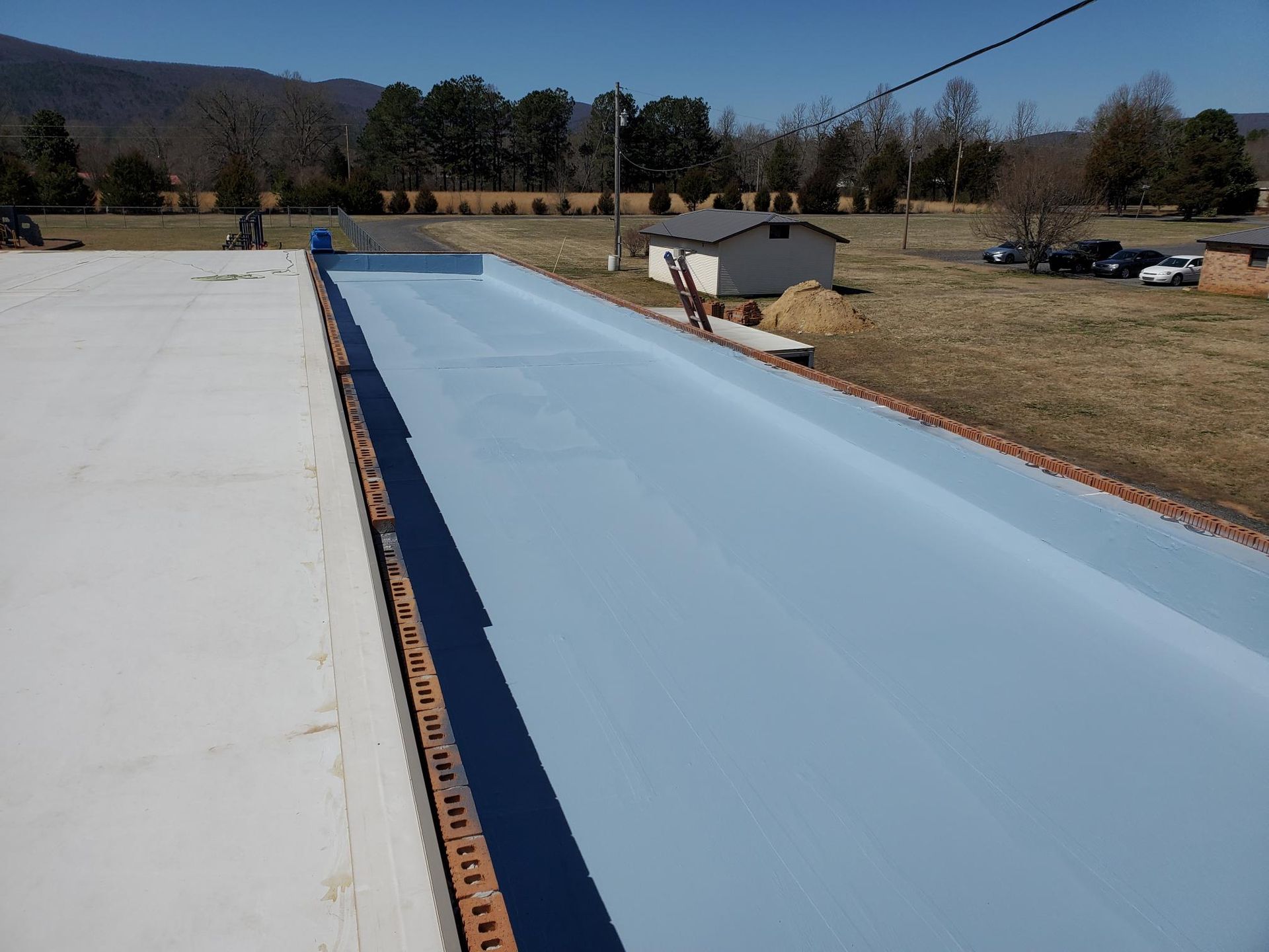 A roof with a ladder on it is being painted blue.