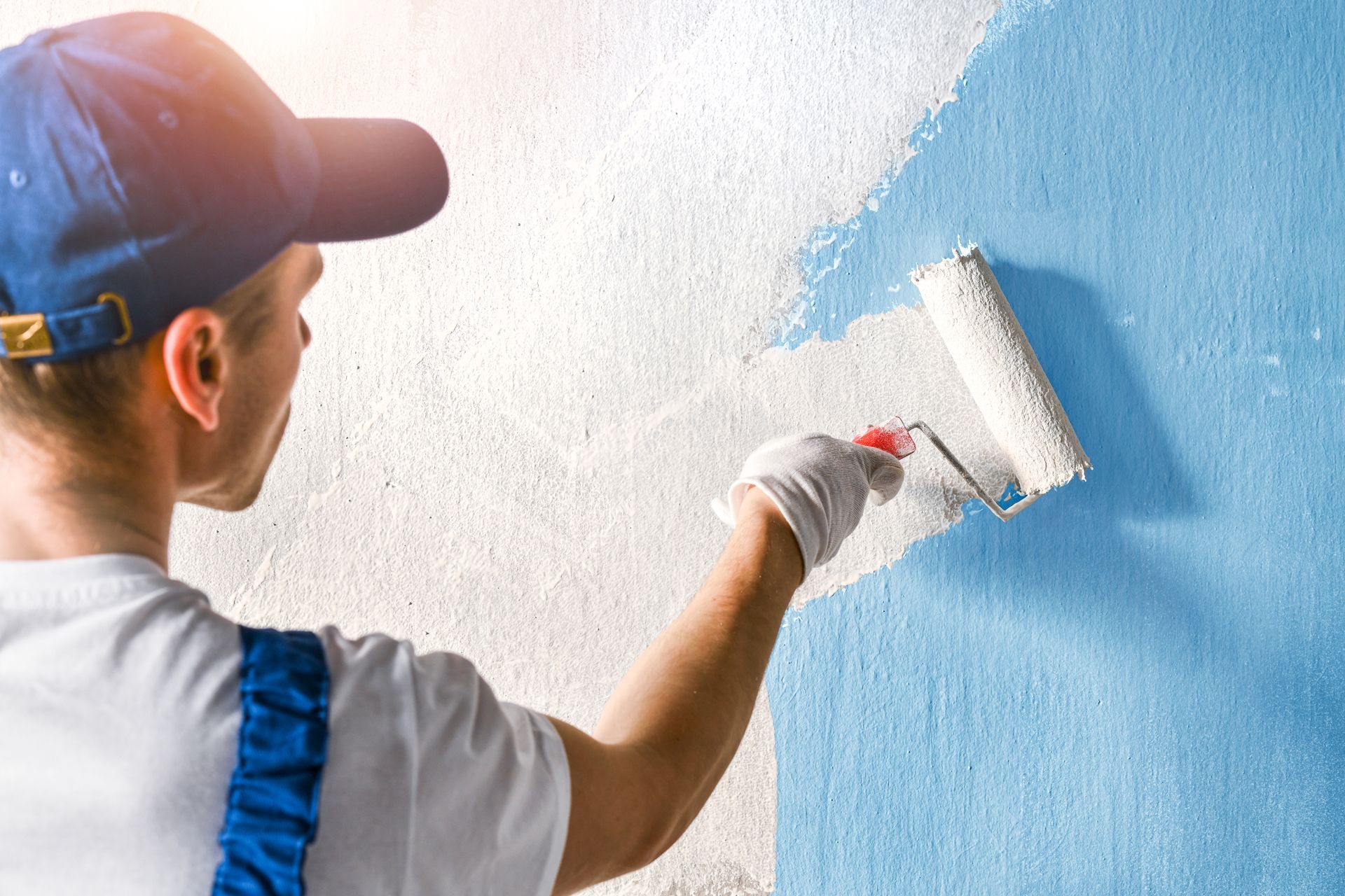 Painter rolling white paint on a wall with a blue section.