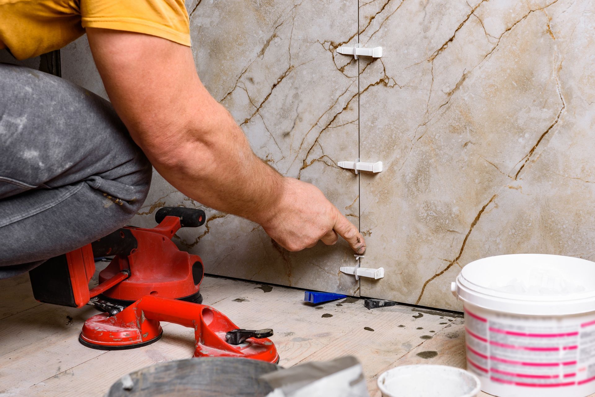 Worker installing wall tiles with spacers and red tools on a tiled floor