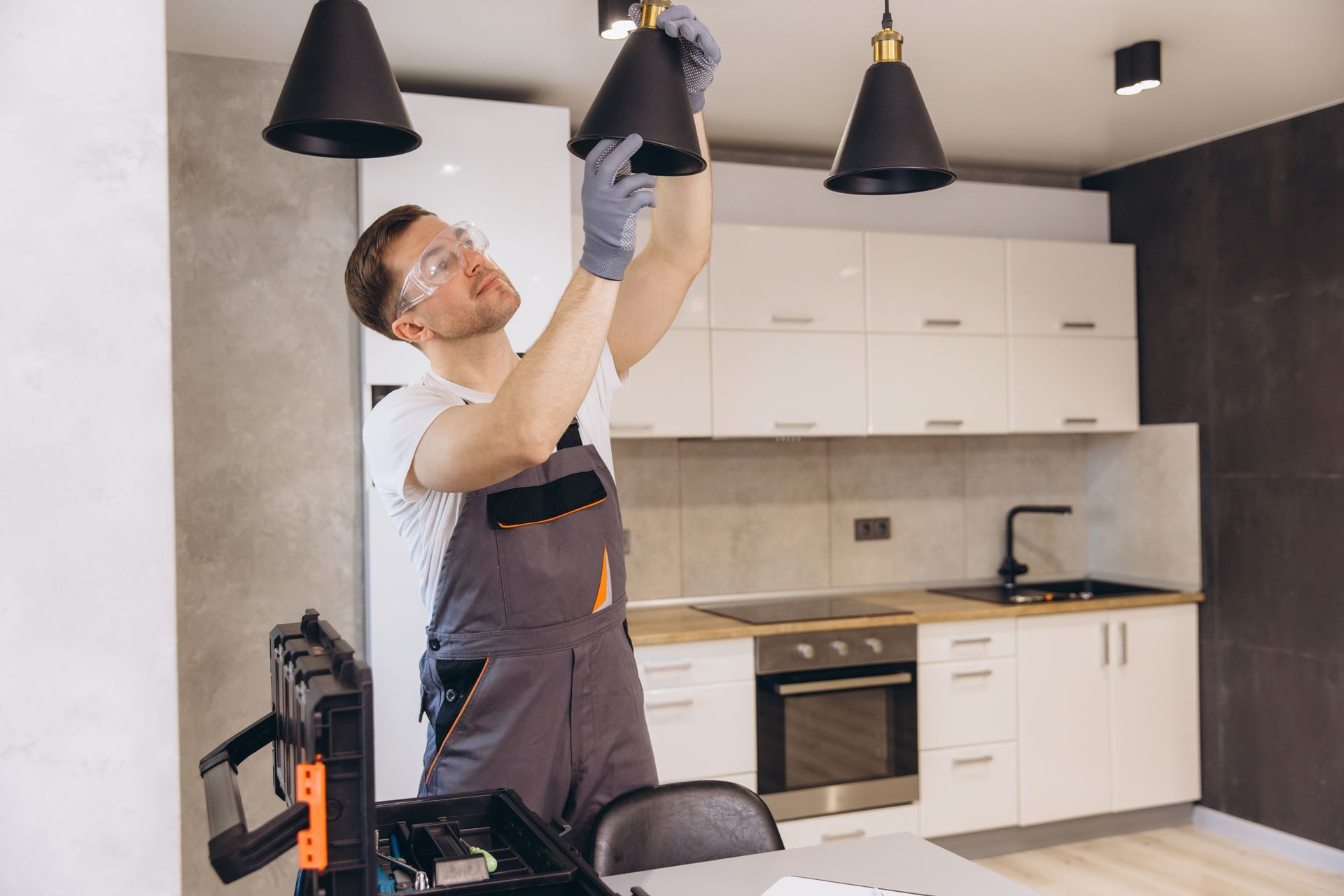 Person adjusting a black pendant light in a modern kitchen with white cabinets