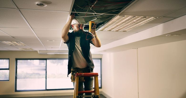 Person on a step ladder working on a dropped ceiling panel in an office room