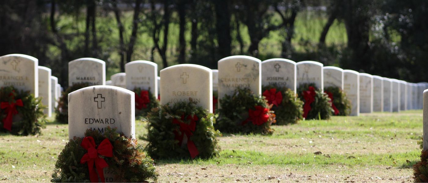 Rows of white military headstones in a cemetery, each decorated with a green wreath and red bow for the holidays.