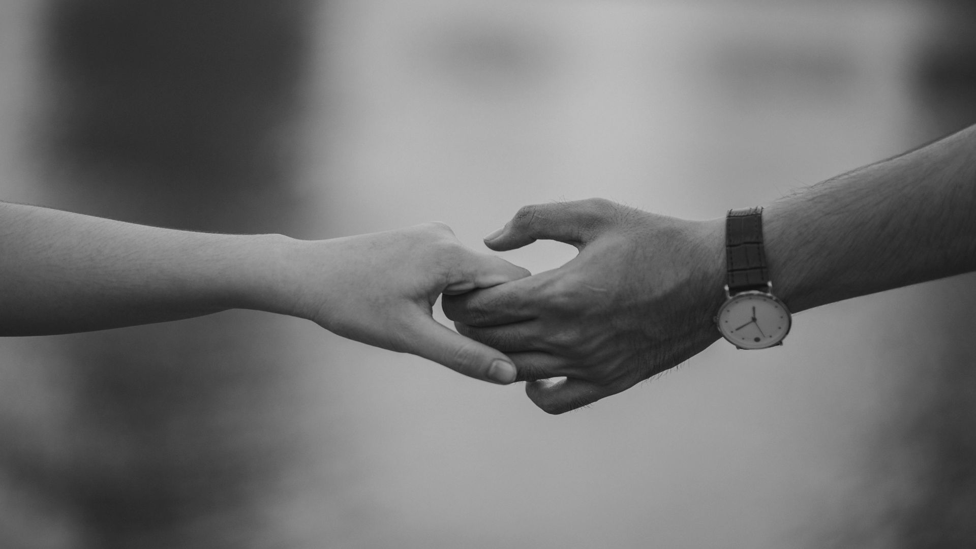 Two hands reaching toward each other in a gentle, close-up hold, captured in black and white.