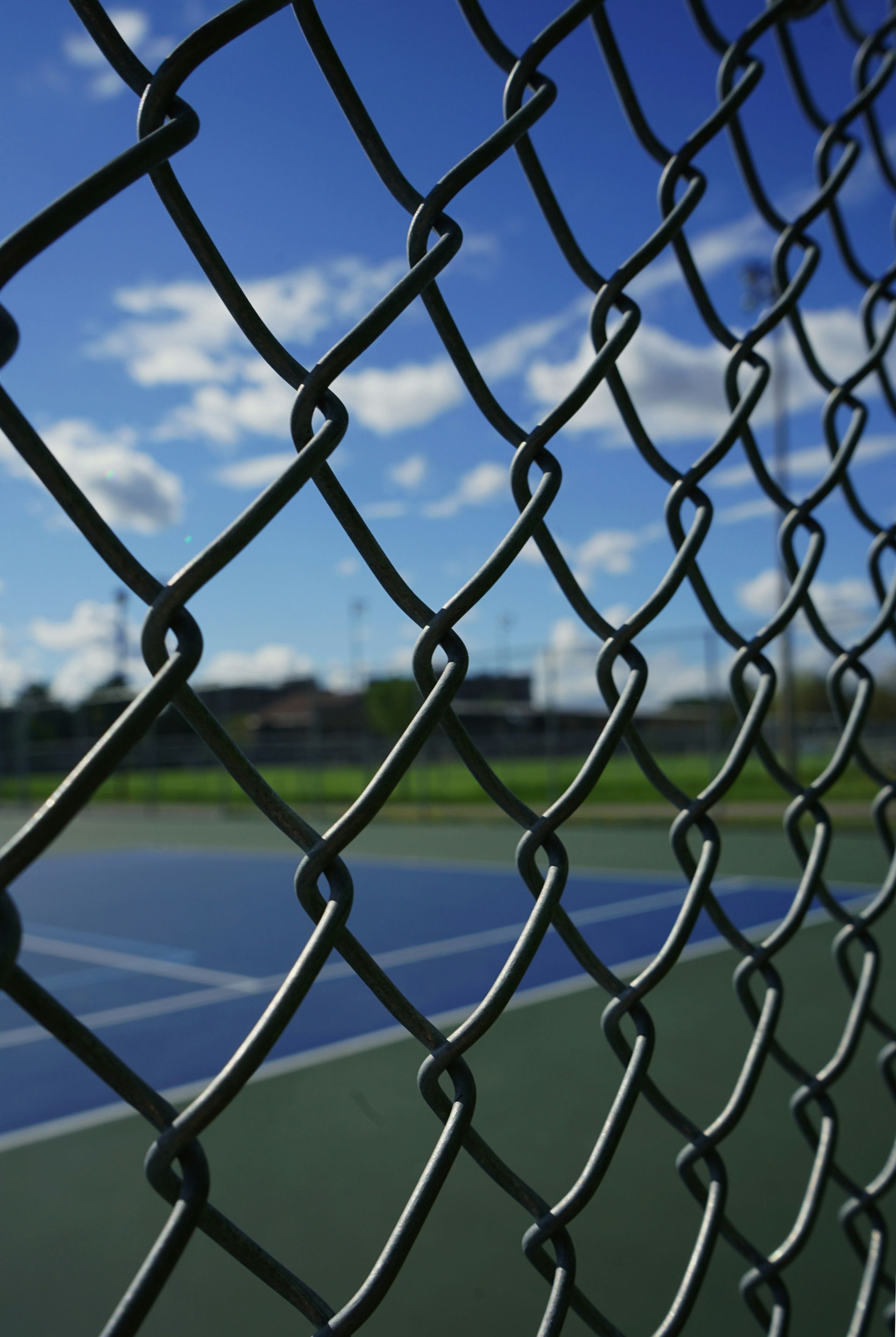 A chain link fence with a tennis court in the background