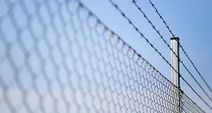A close up of a chain link fence with barbed wire against a blue sky.