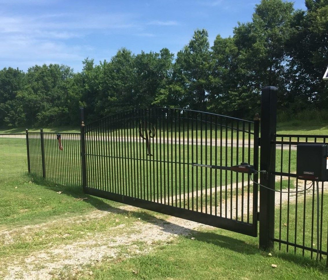 A black fence is surrounding a grassy field with trees in the background.