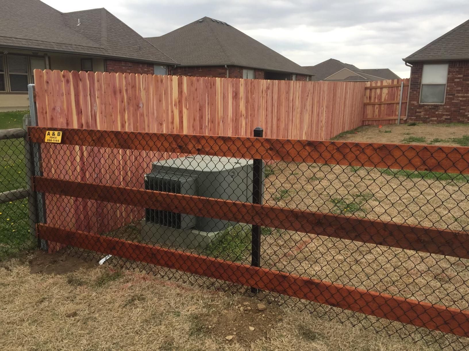 A wooden fence surrounds a chain link fence in a backyard.