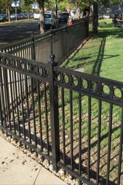 A black wrought iron fence surrounds a park