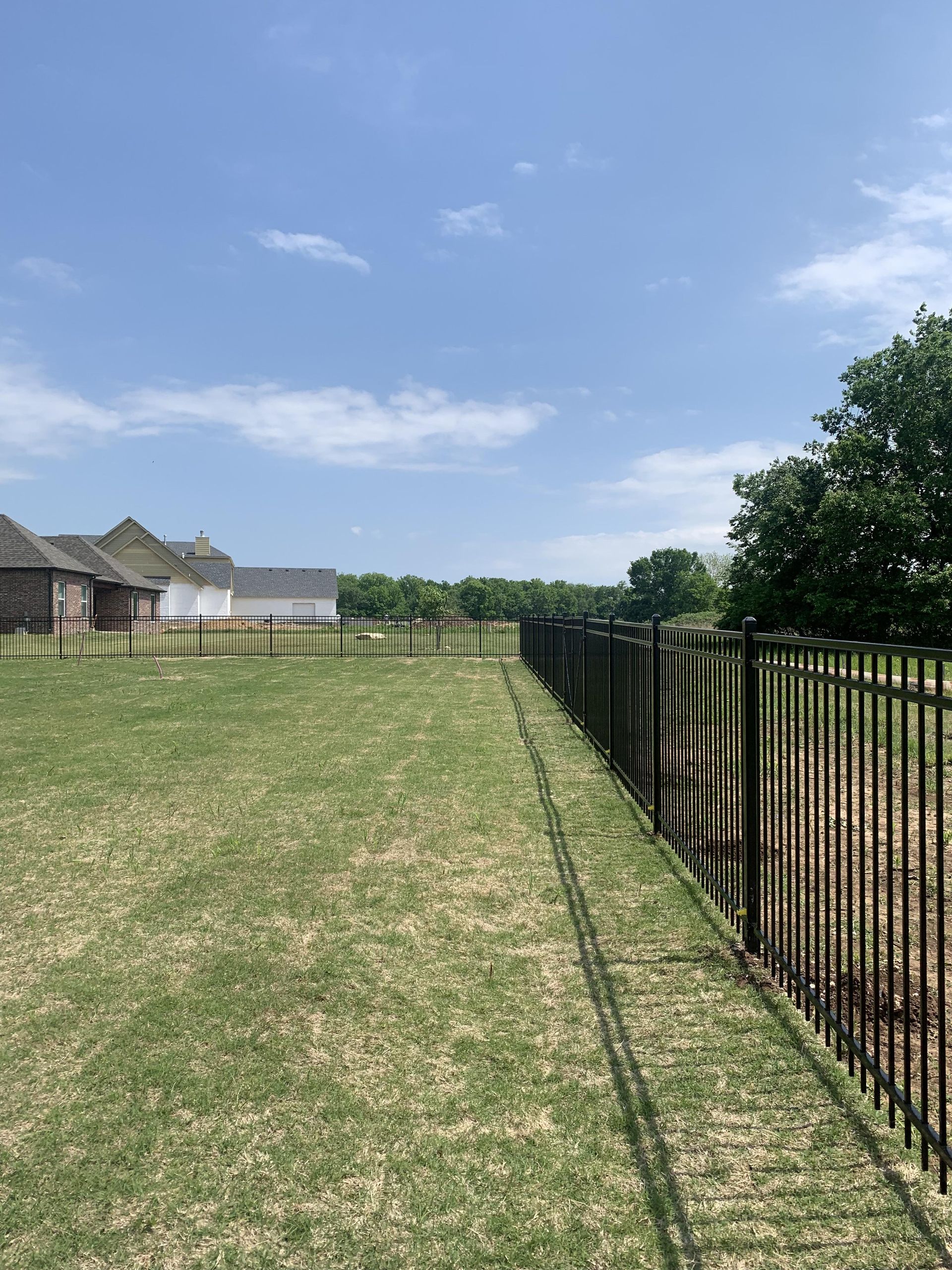 A black metal fence surrounds a lush green field.