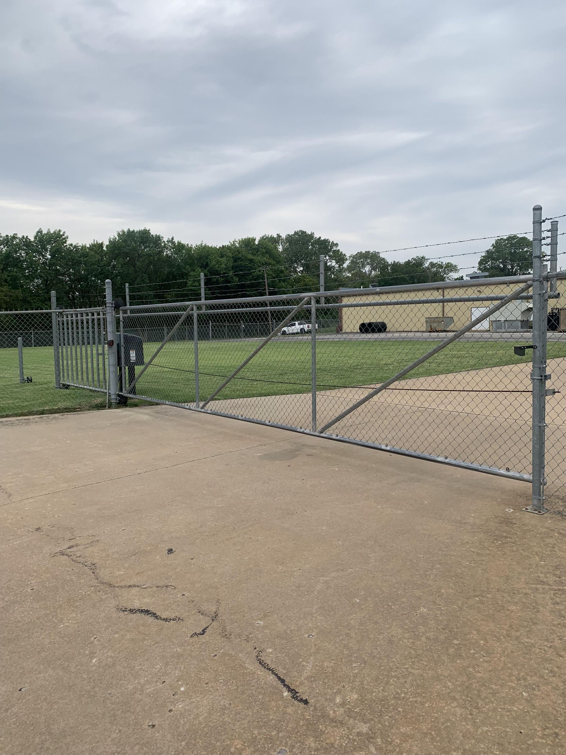 A chain link fence is surrounding a field with a building in the background.