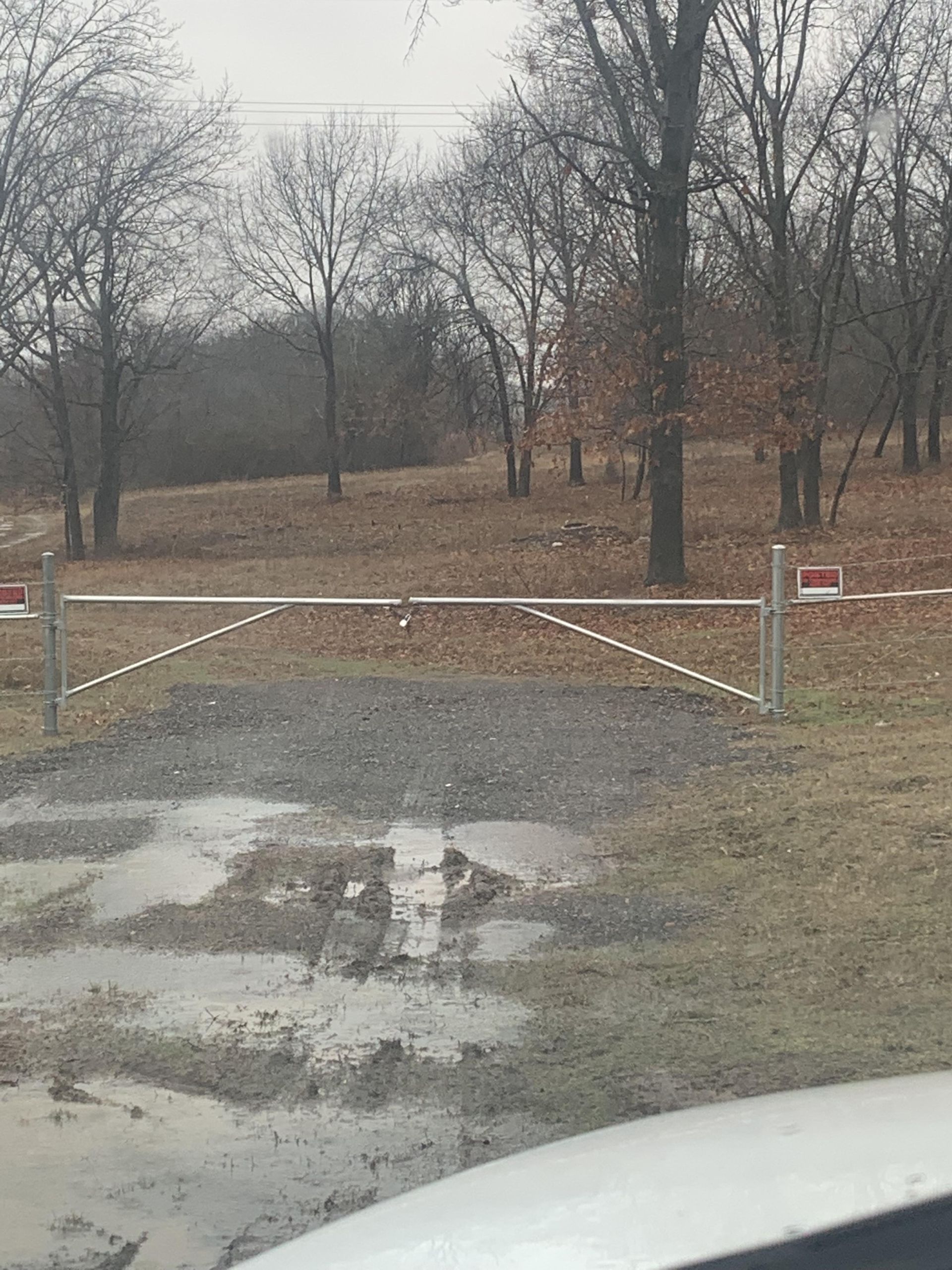 A muddy road with a fence and trees in the background.