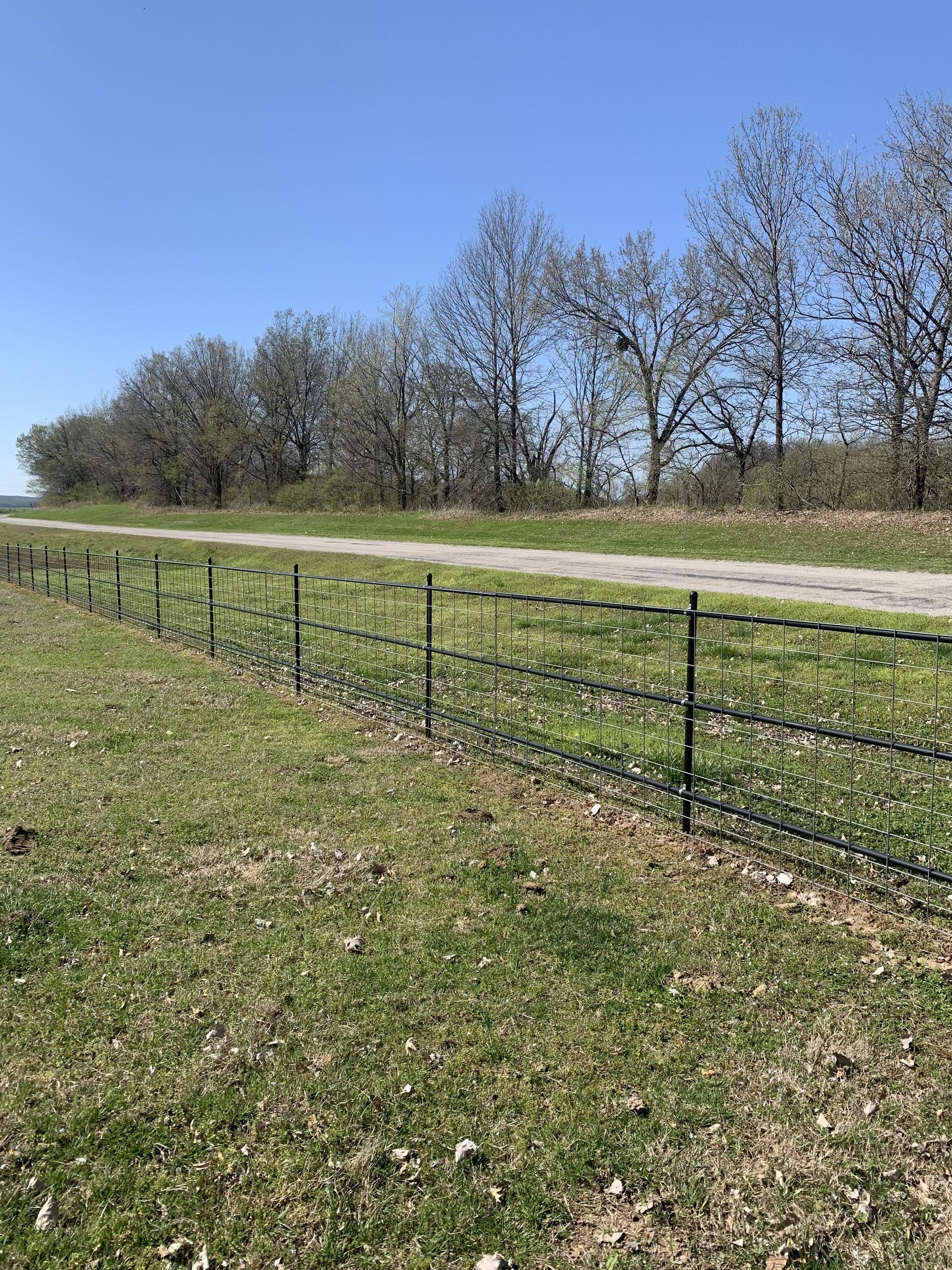 A fence surrounds a grassy field next to a dirt road.