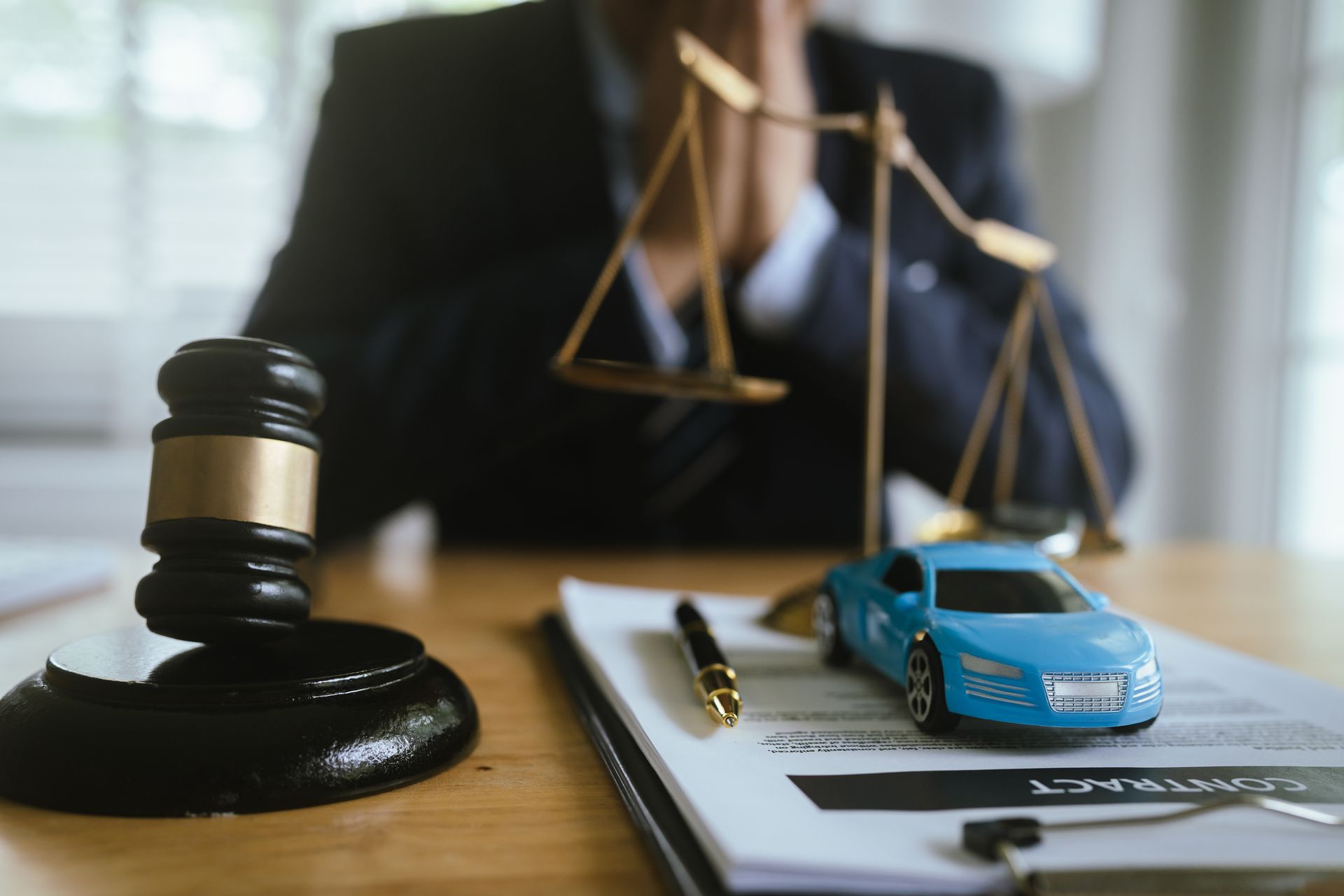 An auto accident attorney is seated in their office with a gavel, scale, and a car on their desk.
