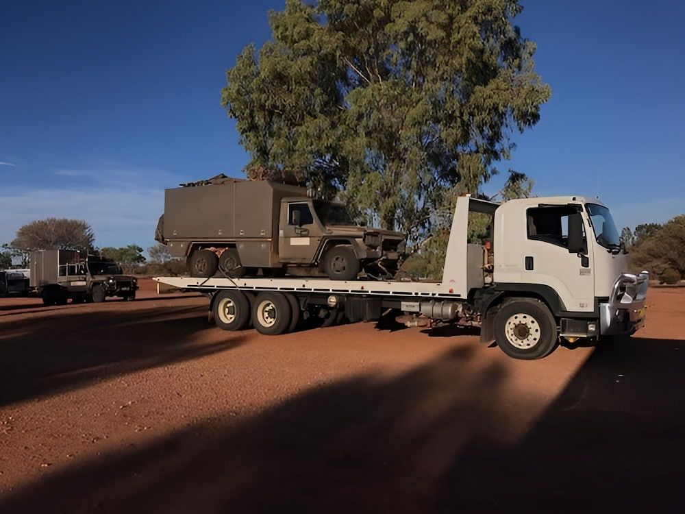 A White Truck Is Carrying A Military Vehicle On Its Flatbed — AHT Towing in Ciccone, NT