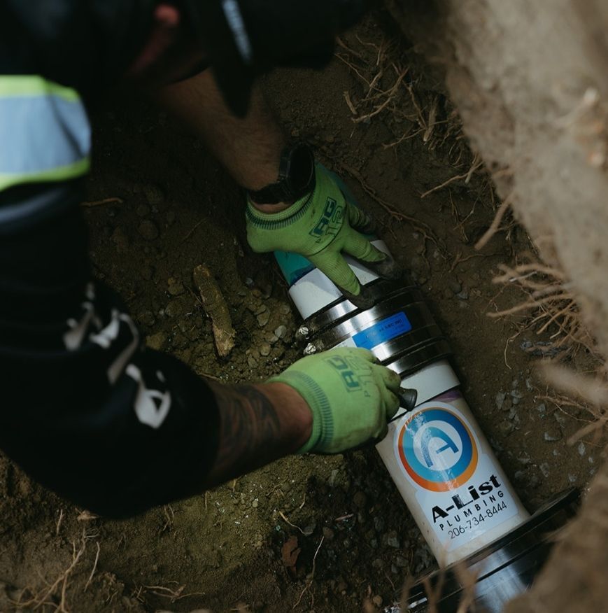 Worker in green gloves connecting a metal pipe in a dirt trench