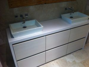 Double-sink bathroom vanity with white basins and drawers against a beige wall