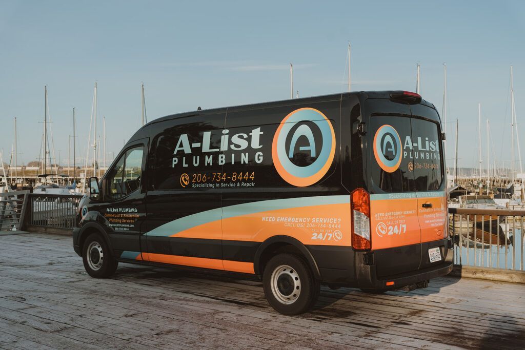 A black and orange A-List Plumbing van is parked in front of a marina.
