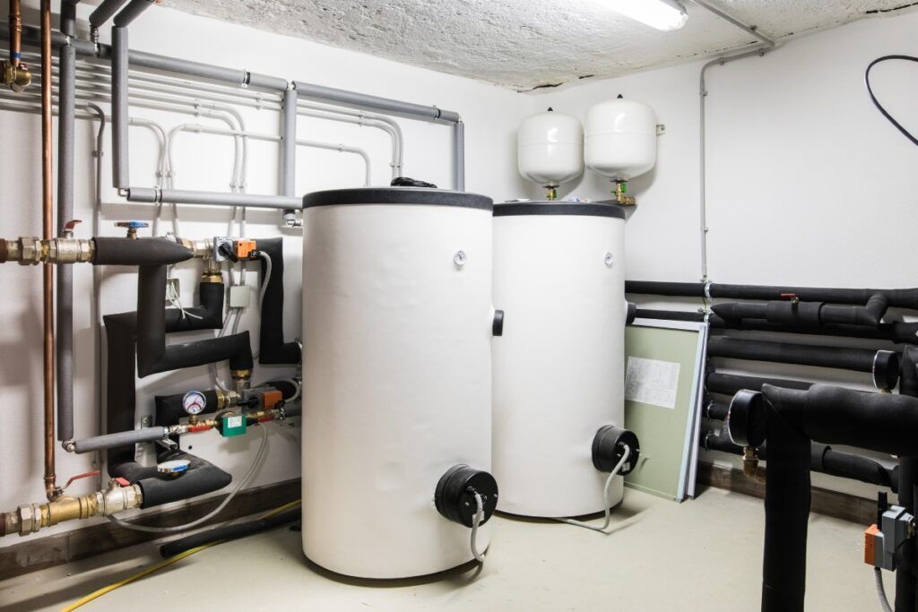 Two water heaters are sitting next to each other in a room with pipes.
