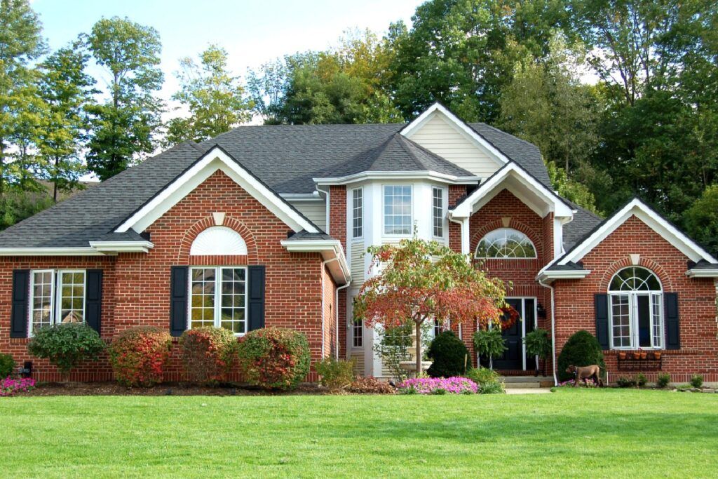 A large brick rental/leased house with a lush green lawn in front of it needing plumbing work