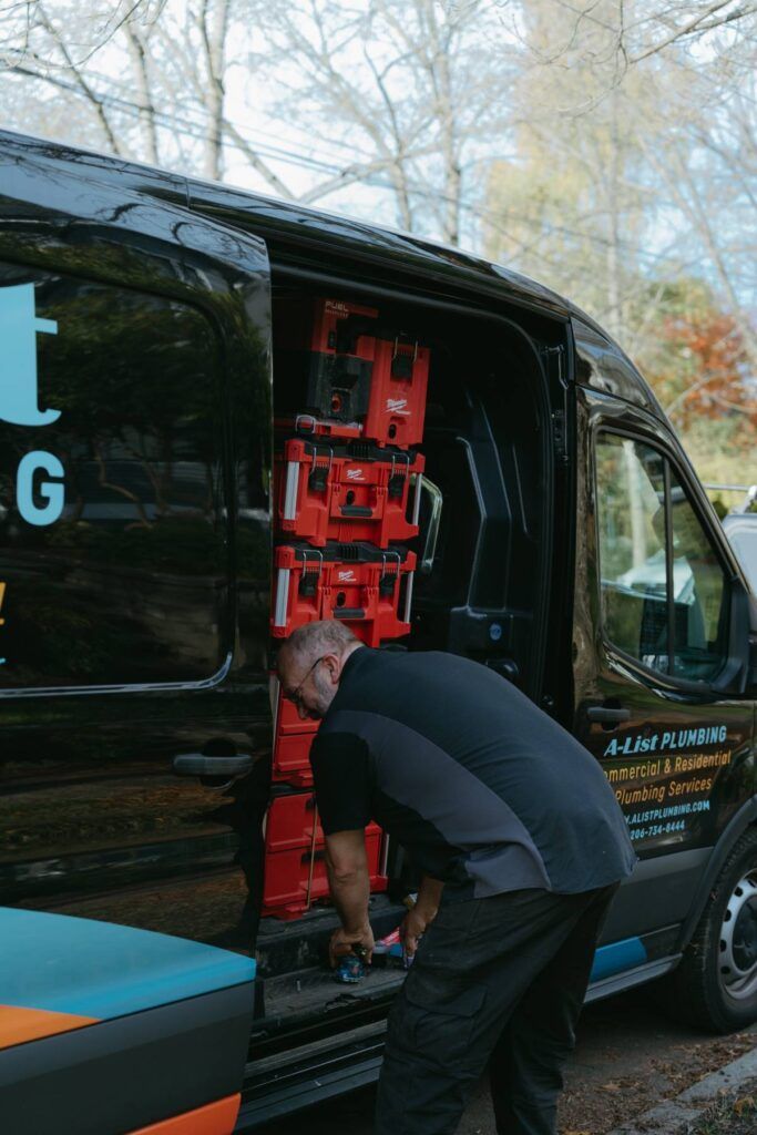 A man is loading tools into the back of a plumbing van.