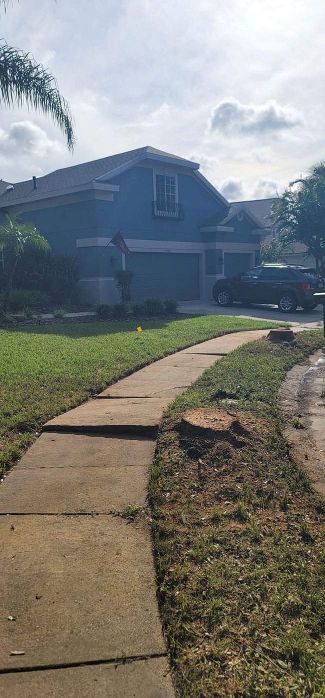 A two-story blue house with a sidewalk in front and green grass. A vehicle is parked in the driveway.