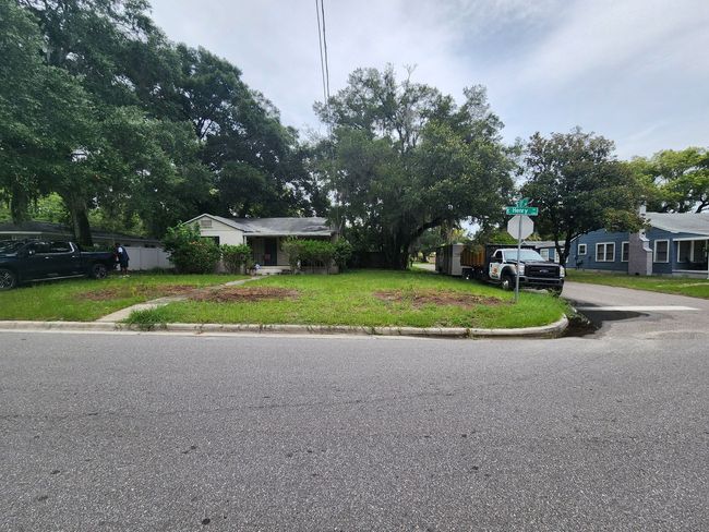 Small house with a yard on a corner lot. A truck is parked in front, grass being cut.
