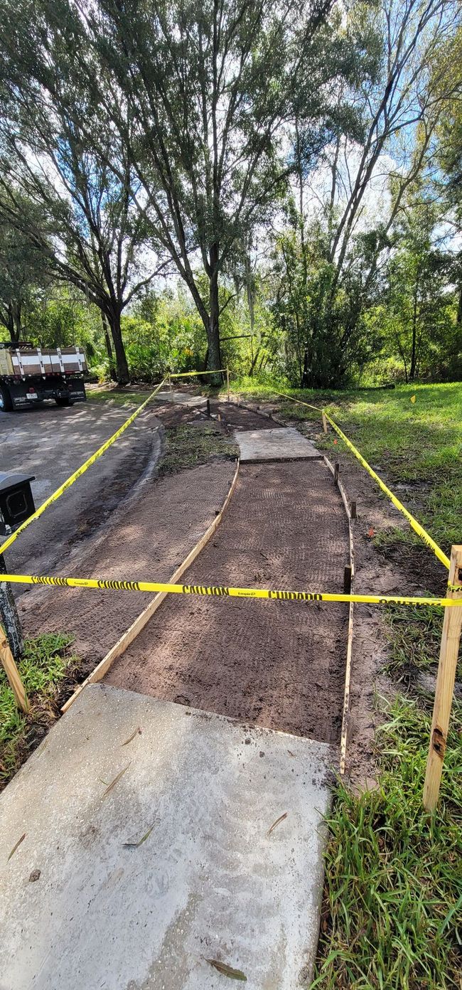 Construction zone with wooden frames, dirt, and caution tape; trees in the background.
