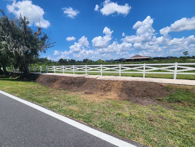 White fence along a road, with grass and blue sky dotted with clouds.