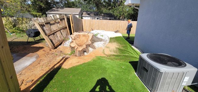 Backyard with a patch of artificial turf, a large rock feature, and a person in the background near a fence.
