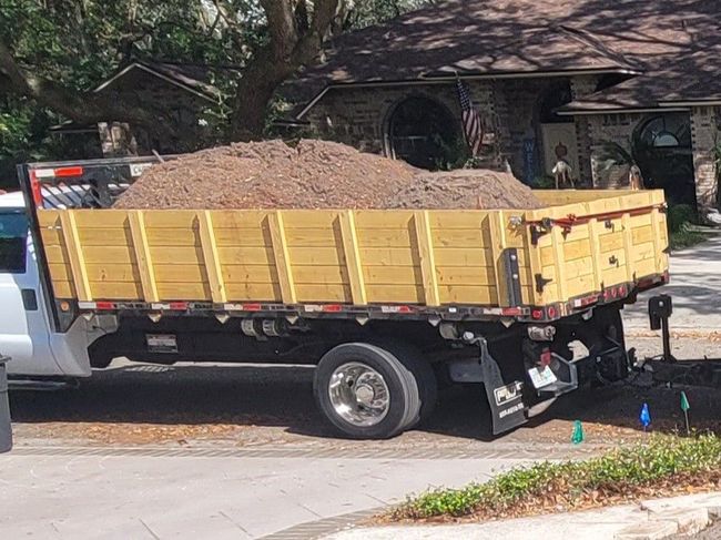 Truck bed filled with dirt parked on a street in front of a house.