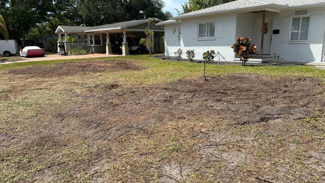 Residential front yards; dry, patchy grass; white house on right, covered parking on left.