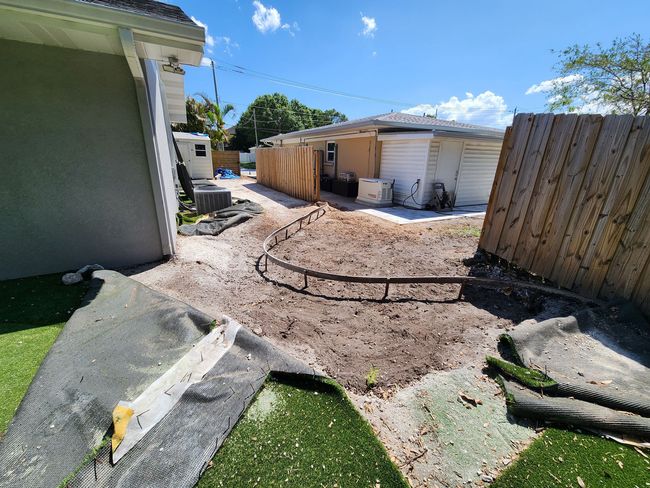Backyard with dirt and debris; a fence and buildings are visible. Artificial turf is on the ground.