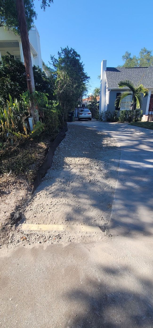 Gravel and paved driveway between houses with a car in the distance under a blue sky.