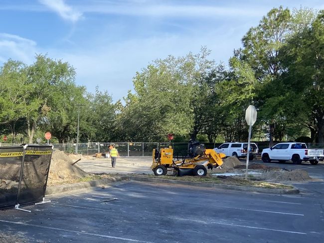 Construction site with a small yellow digger, worker, dirt pile, and white trucks.