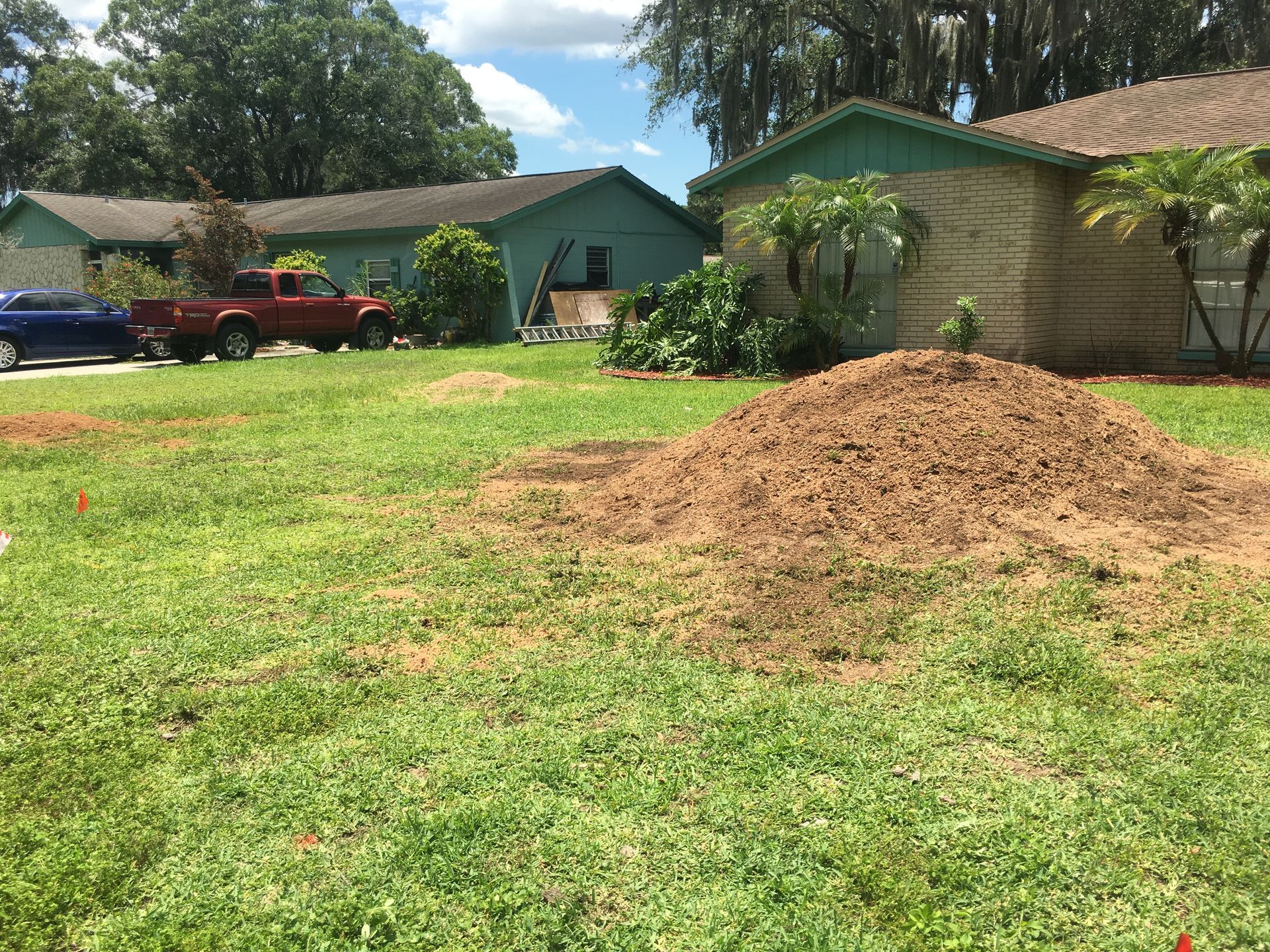 A large pile of wood chips is in the middle of a yard in front of a house.