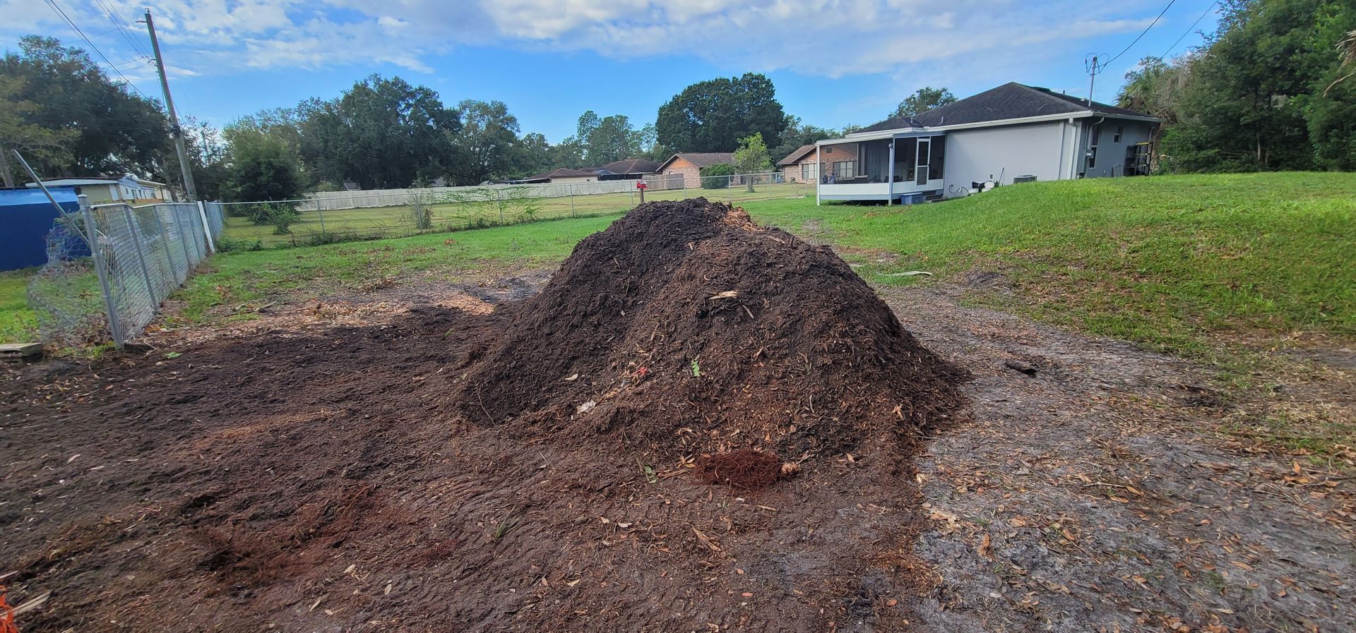 A pile of stump grinding debris is sitting on the side of a dirt road in front of a house.