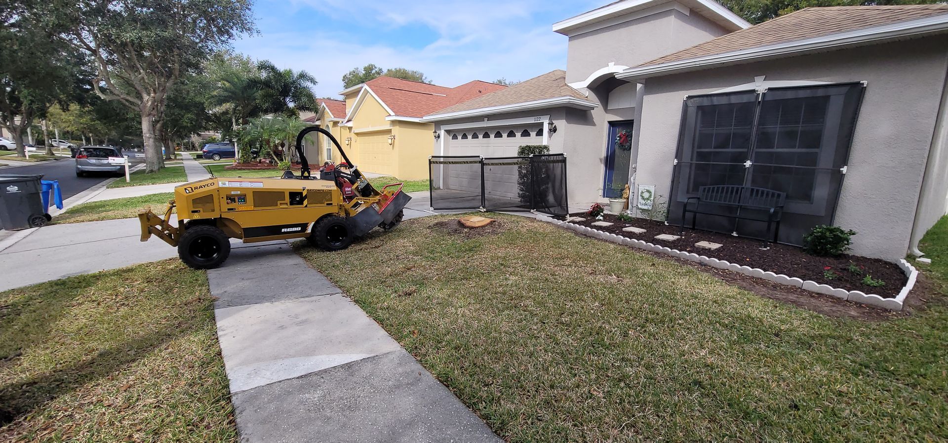 A stump grinder is sitting on the sidewalk in front of a house.