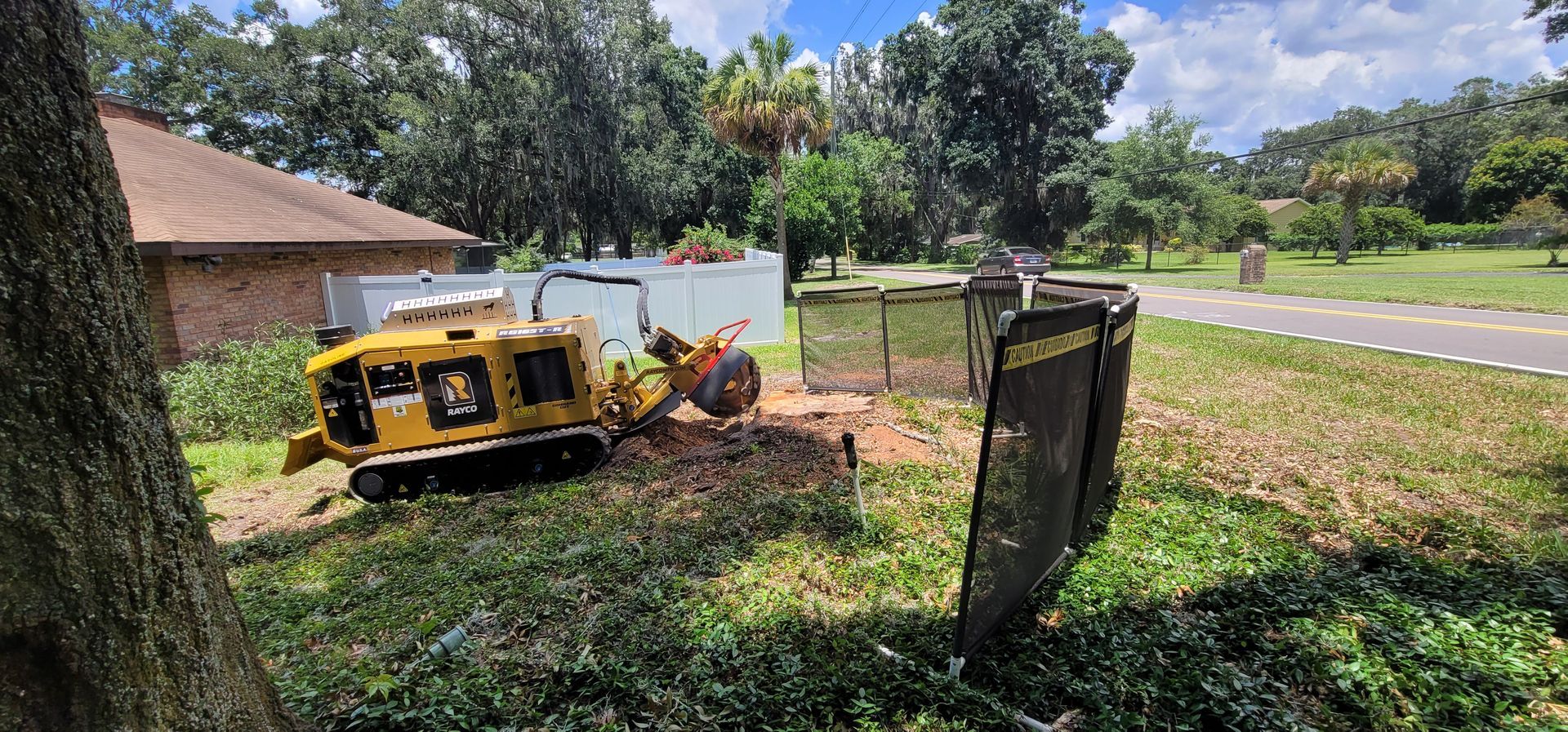 A yellow tractor is cutting down a tree in a yard.