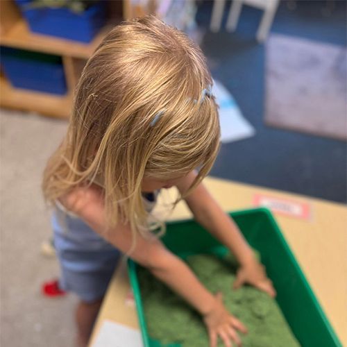 Child pressing hands into green sensory bin in a classroom