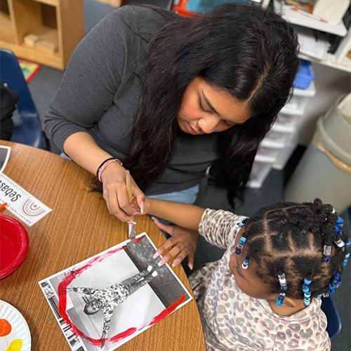 Teacher helping a child with a craft project at a table