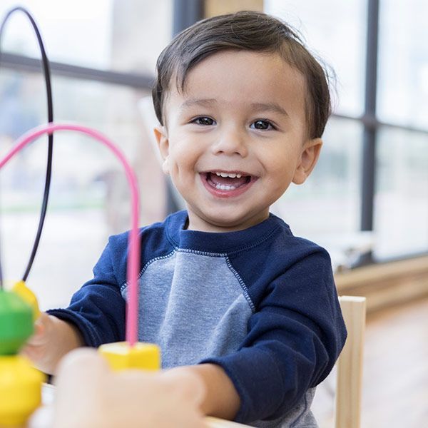 Smiling toddler playing with colorful toys at a table near a bright window